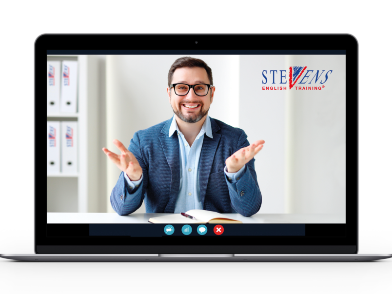 Auf dem Bildschirm eines Laptops ist ein lächelnder Mann in einem Videoanruf zu sehen; er sitzt an einem Schreibtisch mit offenem Buch und gestikuliert mit beiden Händen. Oben rechts im Bild steht das Logo von STEVENS English Training.